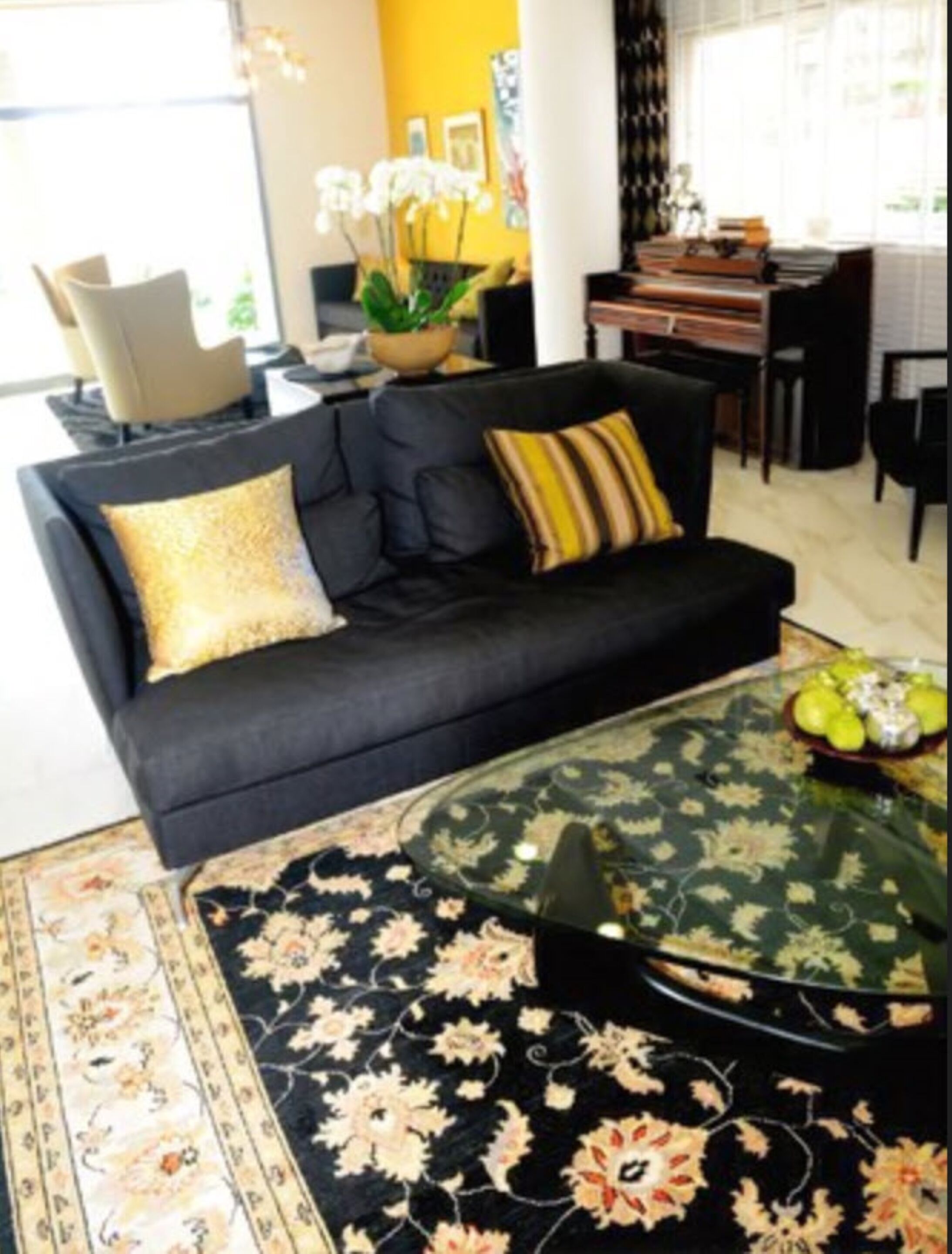 A modern living room with a black sofa, a glass coffee table, and a floral rug.