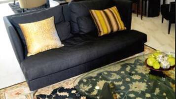 A modern living room with a black sofa, a glass coffee table, and a floral rug.