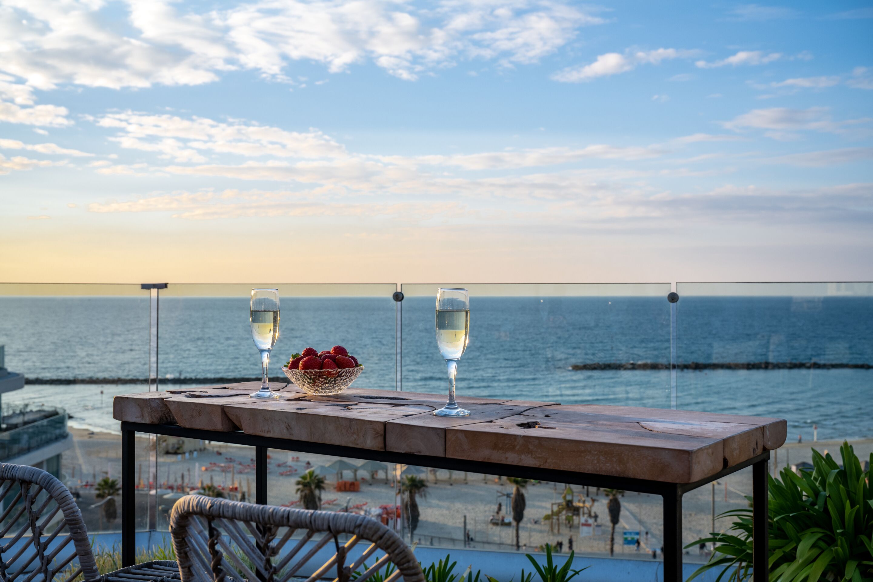 Una mesa con dos copas de vino blanco y un cuenco de fruta en un balcón con vistas al mar.