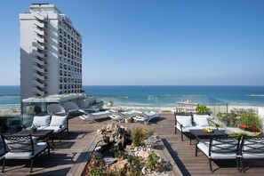 A rooftop terrace with outdoor seating, a view of the ocean, and a hotel building in the background. - Maxim Hotel Tel Aviv (Tel Aviv)