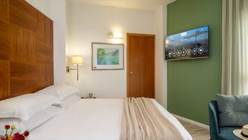 Una habitación de hotel con una cama, televisión montada en la pared, cabecero de madera, pared de acento verde y un sillón azul.