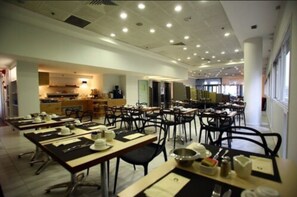 A spacious dining area with multiple tables and chairs, a kitchen in the background, and a bright, well-lit interior. - Maxim Hotel Tel Aviv (Tel Aviv)