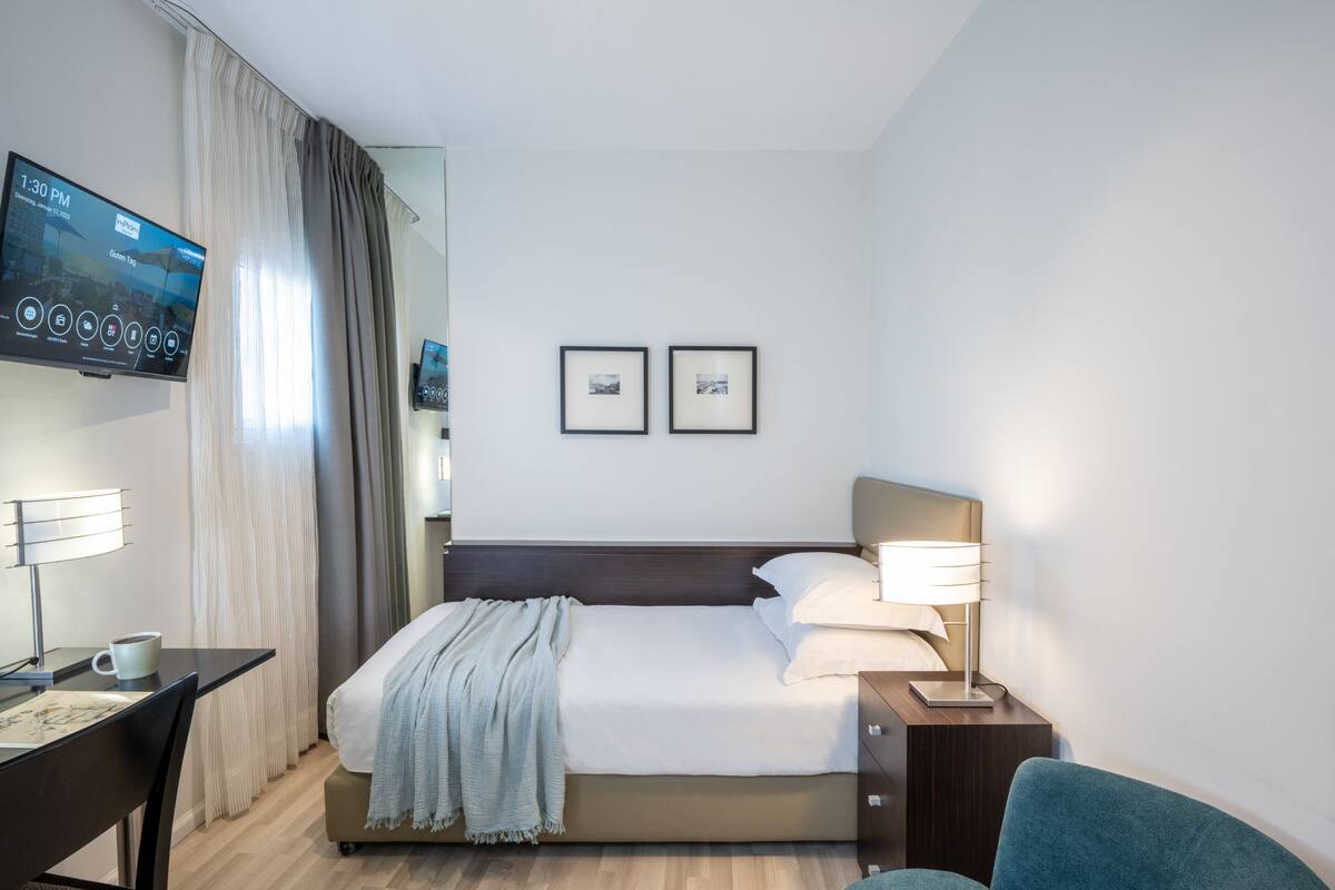 Una habitación de hotel con una cama, un escritorio, una silla, un televisor y dos cuadros en la pared.
