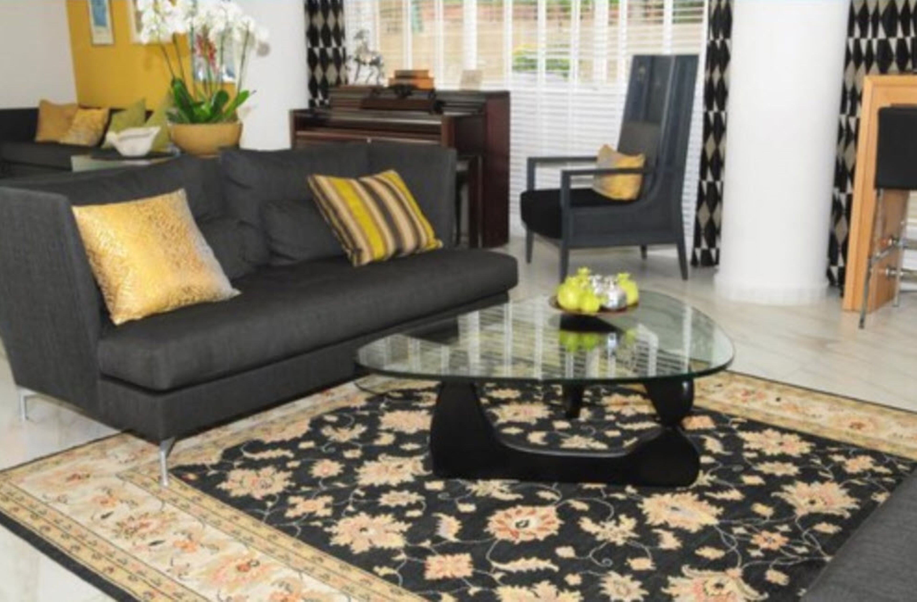 Un salon avec un canapé, une table basse en verre et un tapis à motifs.