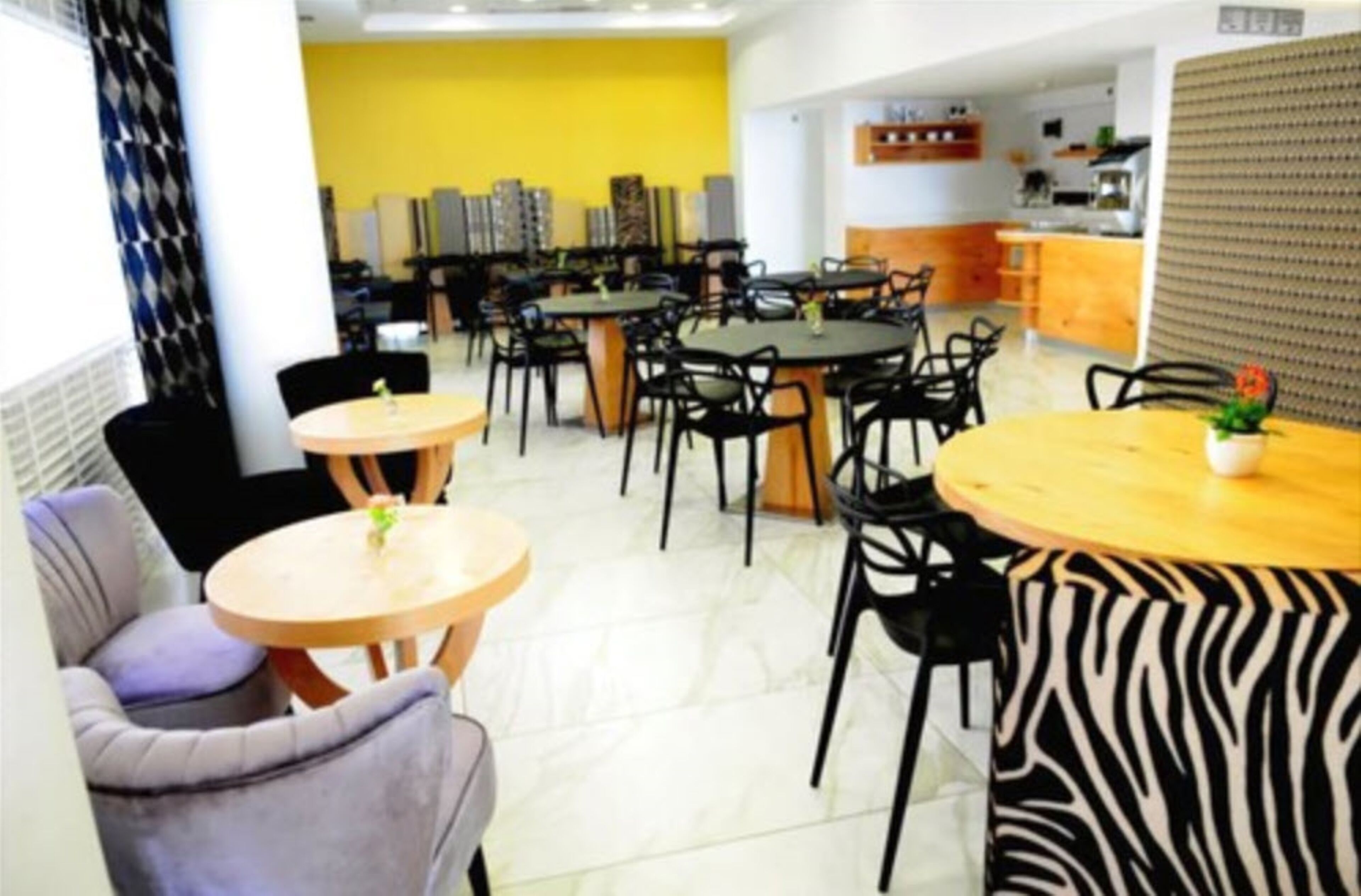 A dining area with multiple tables and chairs, a kitchen in the background, and a yellow wall.