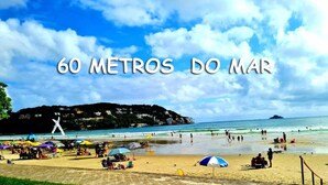 A beach with umbrellas and people, and the text "60 METROS DO MAR".