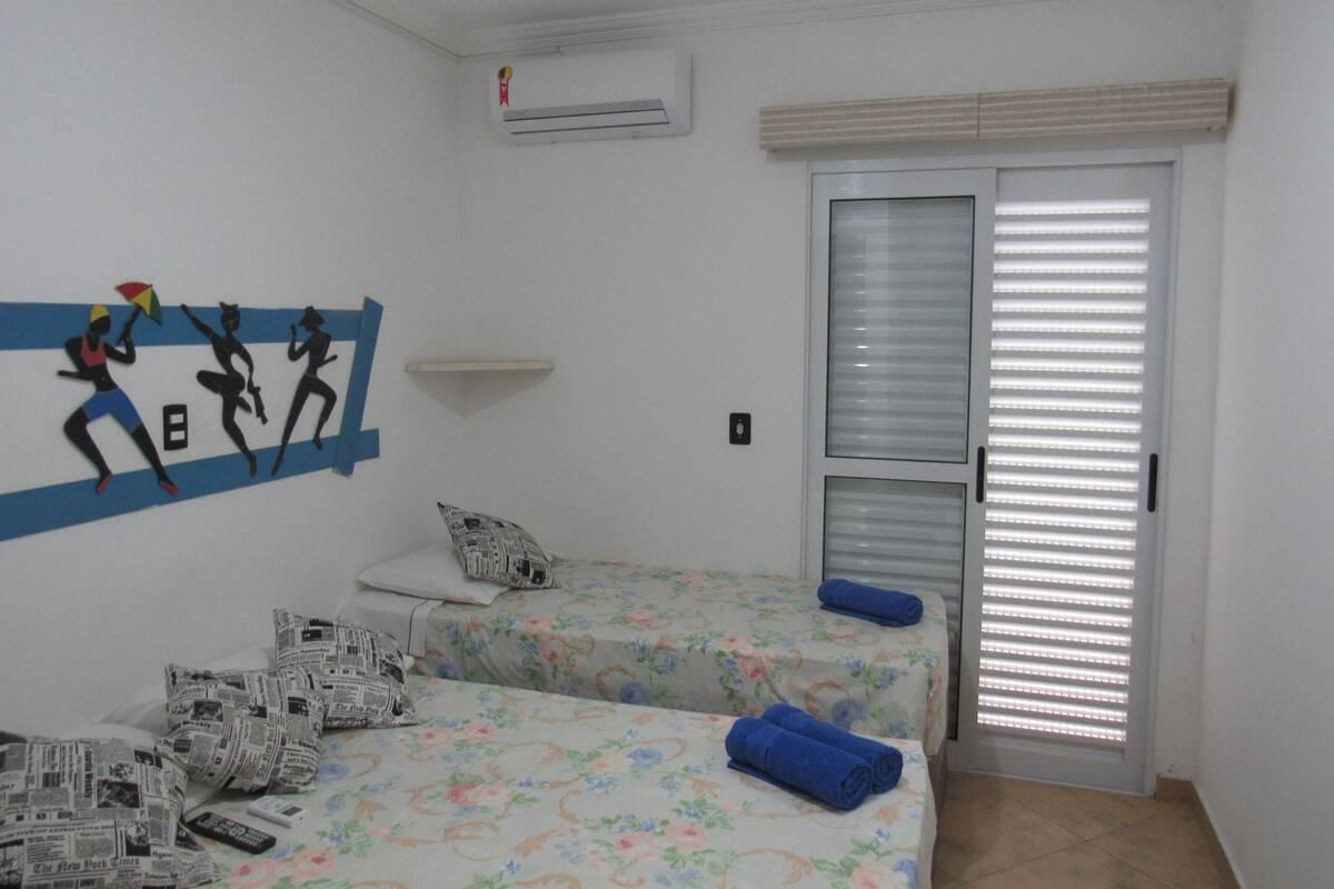 Une chambre avec deux lits, une décoration murale, un climatiseur et une porte avec des stores.