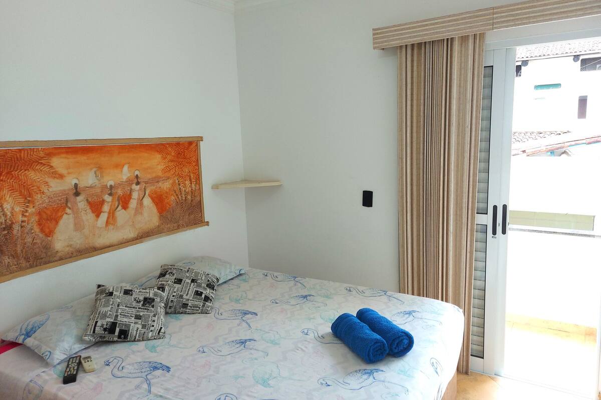 Une chambre d’hôtel avec un lit, un tableau au mur, une petite étagère et une vue sur l’extérieur, visible à travers la porte.
