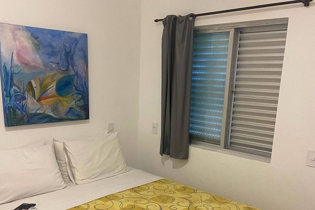 Une chambre à coucher avec un lit, un tableau, une fenêtre avec des stores et un appareil de climatisation.