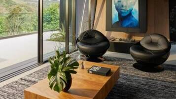 A modern living room with a large window, a wooden coffee table, two black chairs, and a painting on the wall.