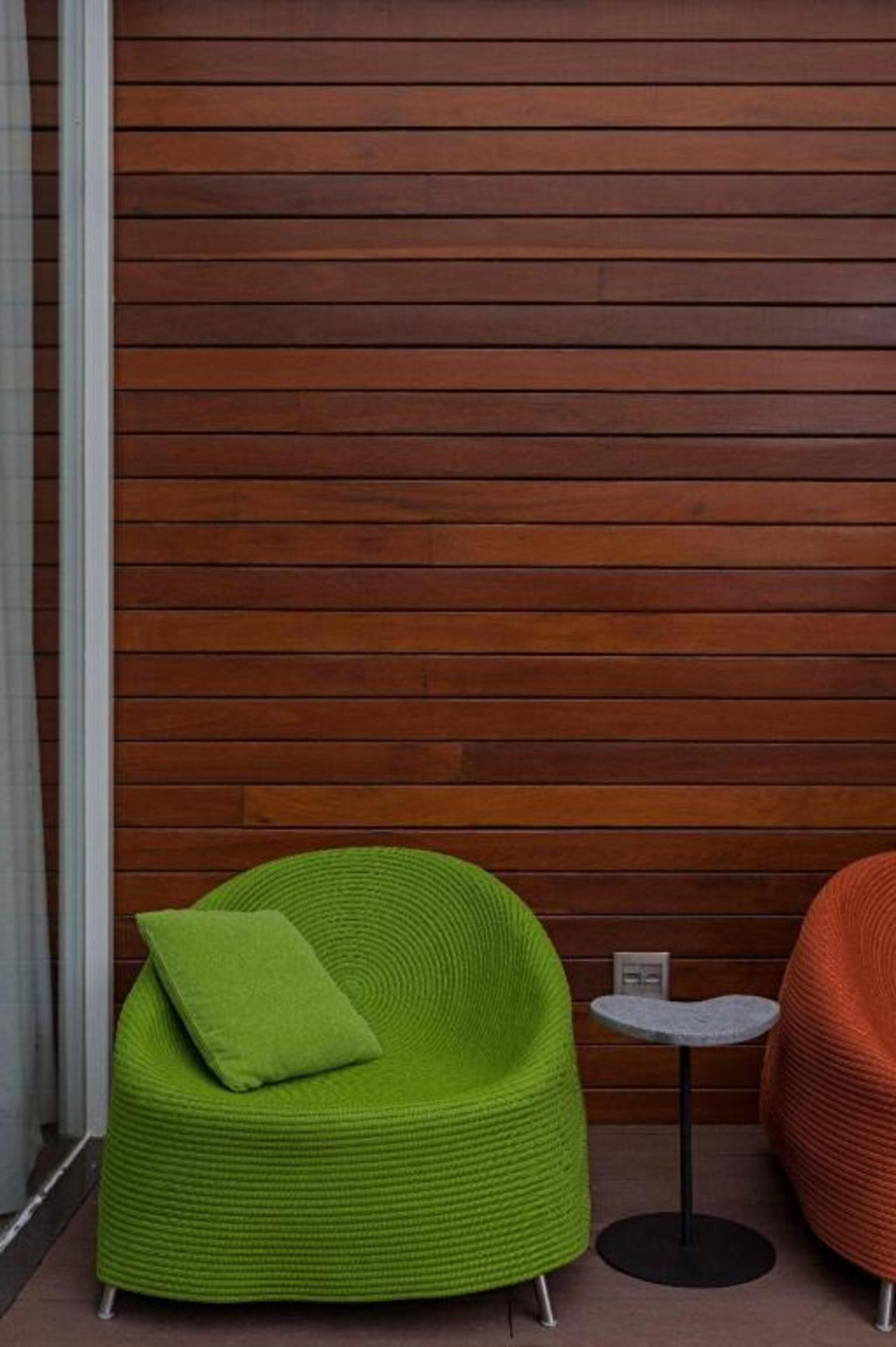 A green chair with a cushion, a small round table, and a red chair against a wooden wall.