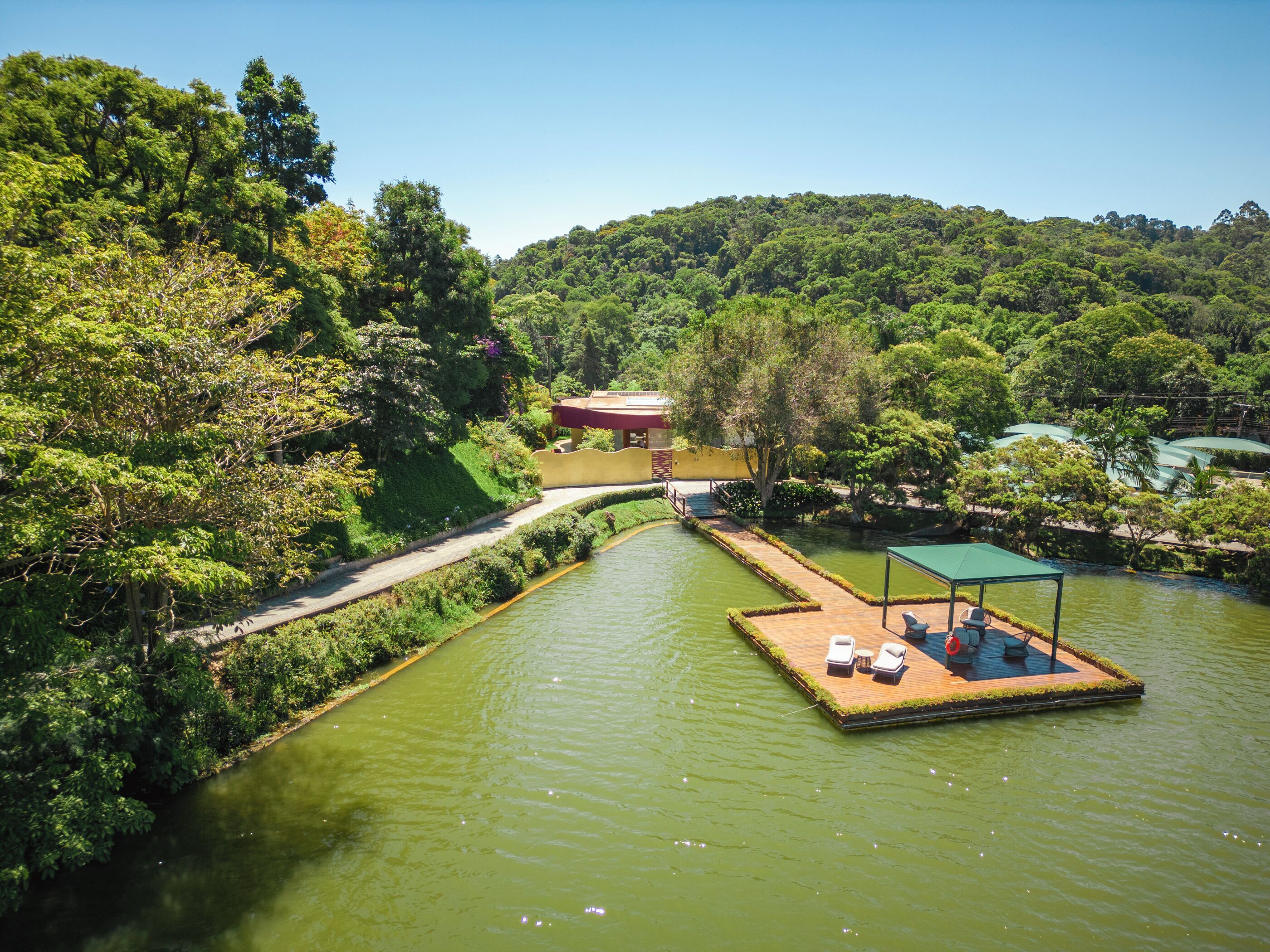 A riverside hotel with a floating deck, a pathway, and lush greenery.