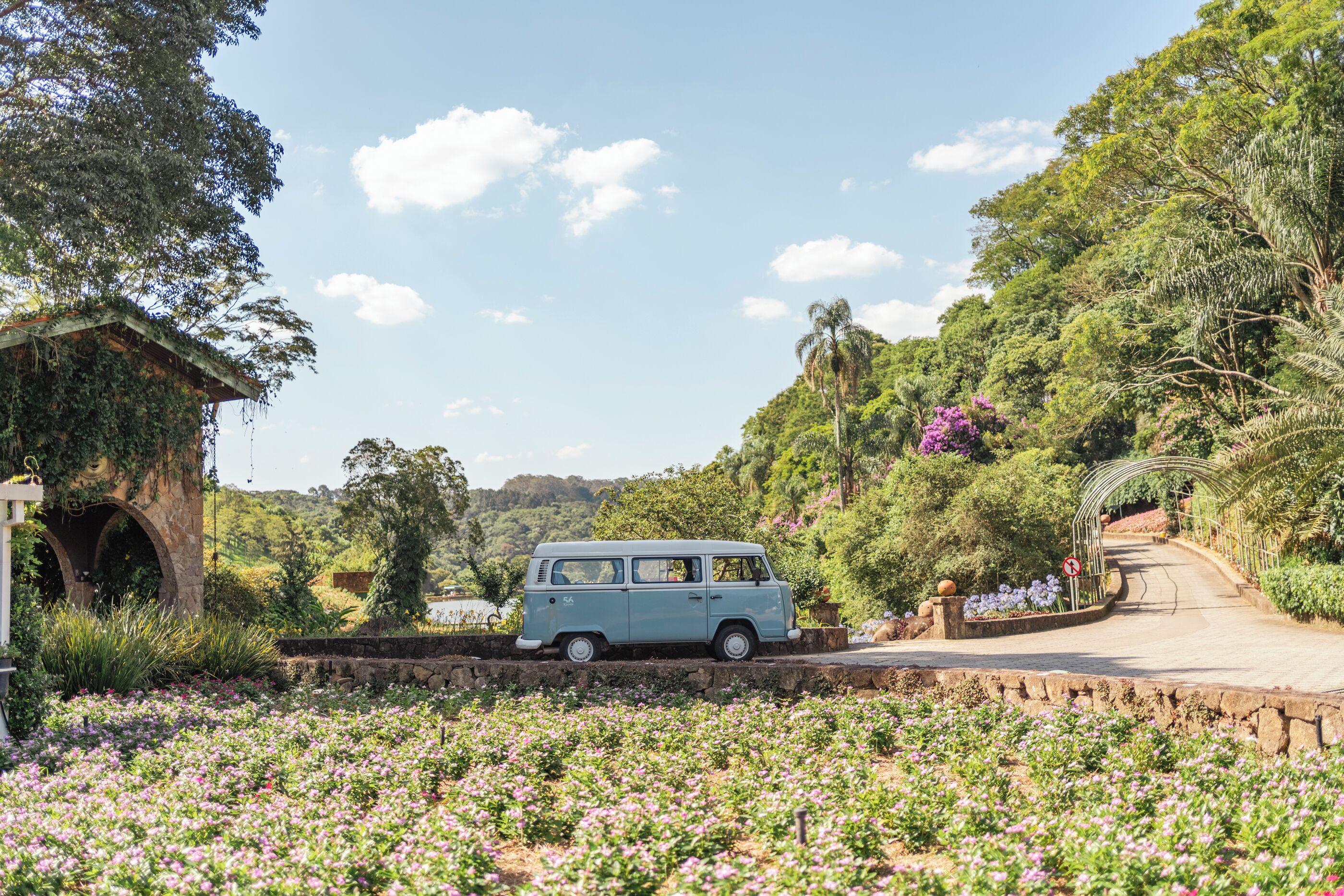 Uma van azul estacionada em um jardim com flores e uma estrutura de pedra.