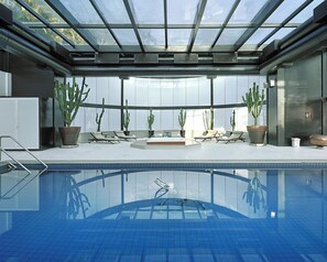 A modern indoor pool with clear glass ceilings, multiple lounge chairs, and potted cacti. - Hotel Unique Garden (Mairipora)