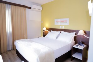 A hotel room with a large bed, two bedside lamps, a nightstand, an air conditioning unit, and a painting on the wall. - Bristol Centro Cívico Multy Hotel (Curitiba)