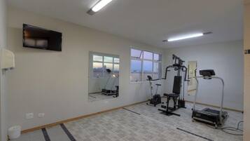 A gym with exercise equipment, large windows, and a flat-screen TV on the wall.