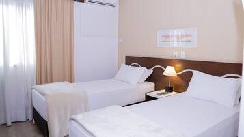 Una habitación de hotel con dos camas, una mesita de noche con lámpara, un equipo de aire acondicionado y un cuadro enmarcado en la pared.