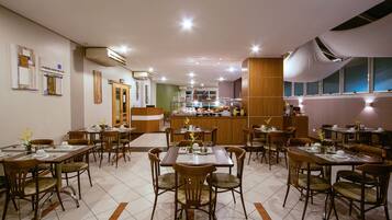 A restaurant with multiple dining tables and chairs, a kitchen area, and a bar.
