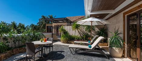 Un patio al aire libre con una mesa redonda, dos sillones de descanso y una planta en maceta.