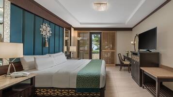 A hotel room with a large bed, a desk with a lamp, a television, and a view of the outdoors through a door.
