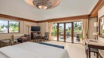 A hotel room with a large bed, a desk, a TV, and a view of palm trees through the windows.