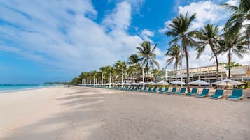 Di pantai, pasir putih, payung pantai, dan handuk pantai