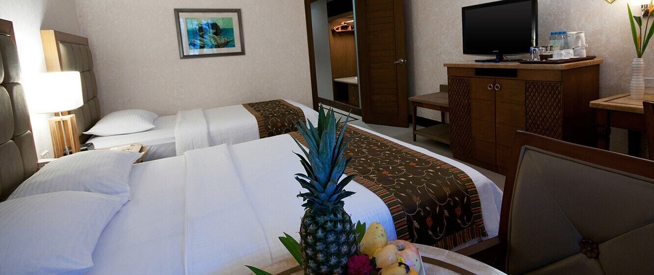 A hotel room with two beds, a television, a desk, and a mirror.