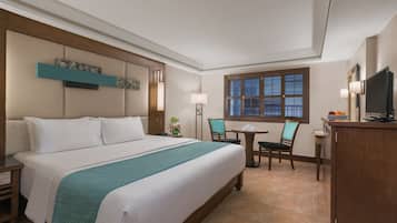 Una habitación de hotel con una cama grande, un escritorio con silla, una mesita y un televisor.