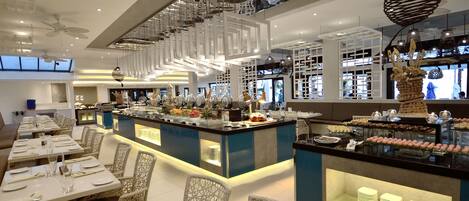 A modern restaurant with a buffet bar, high ceilings, and contemporary lighting fixtures.