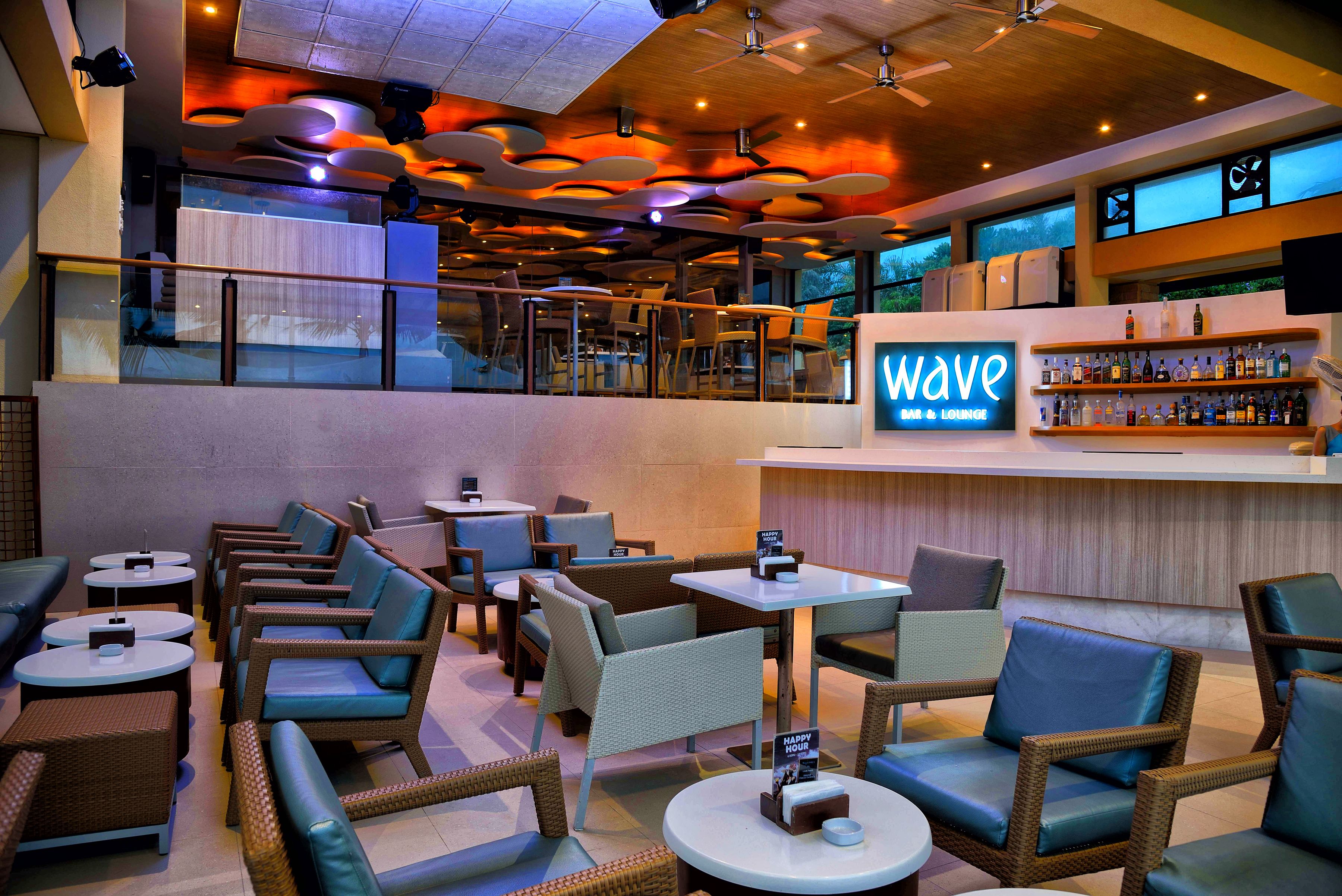 A bar/lounge area with wicker furniture, a bar counter, and a sign reading "Wave Bar & Lounge".