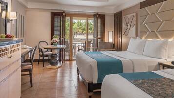 A hotel room with two beds, a dining area, and a view of palm trees.