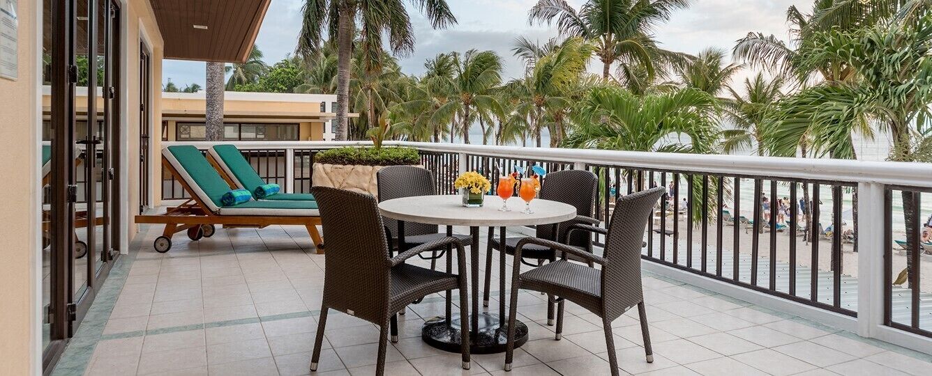 A balcony with a table and chairs, a sun lounger, and a view of the beach.