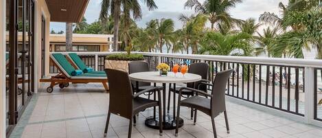 A balcony with a table and chairs, a sun lounger, and a view of the beach.