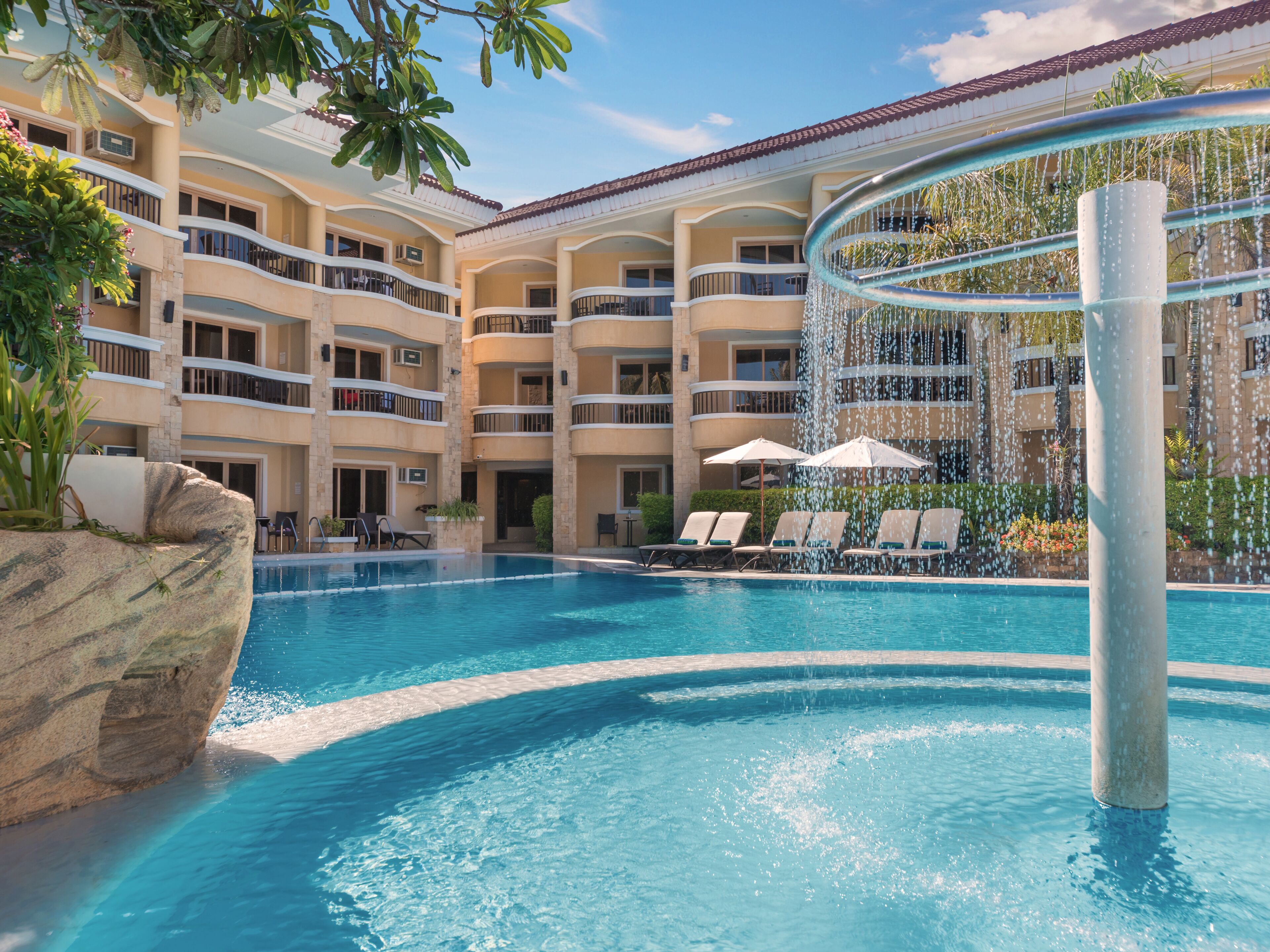 A hotel with a swimming pool, lounge chairs, and a water feature.