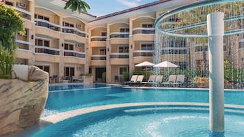 A hotel with a swimming pool, lounge chairs, and a water feature.