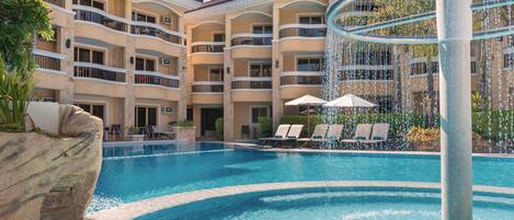 A hotel with a swimming pool, lounge chairs, and a water feature.