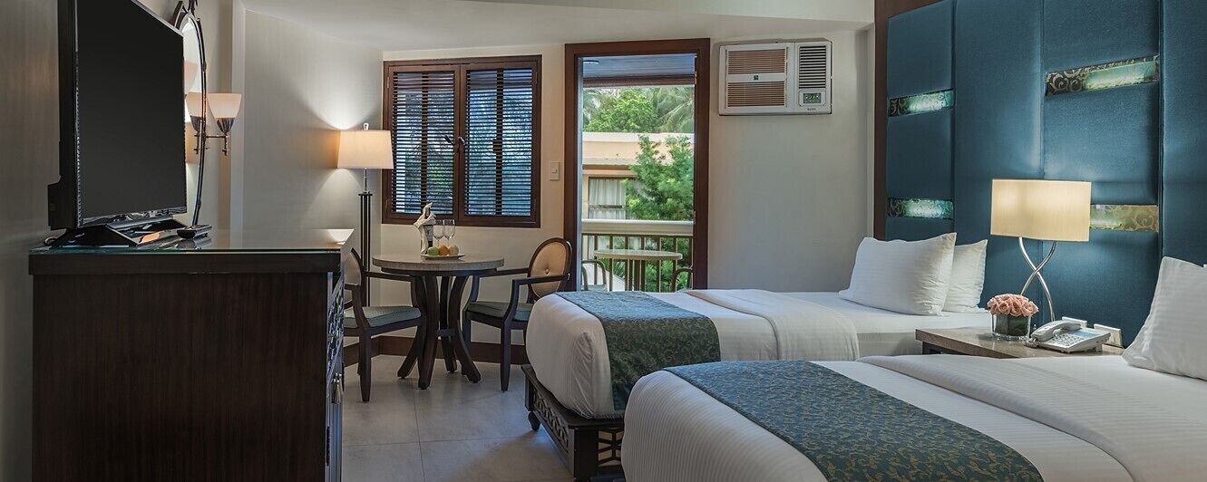 A hotel room with two beds, a desk, a chair, a TV, and a balcony with a view.