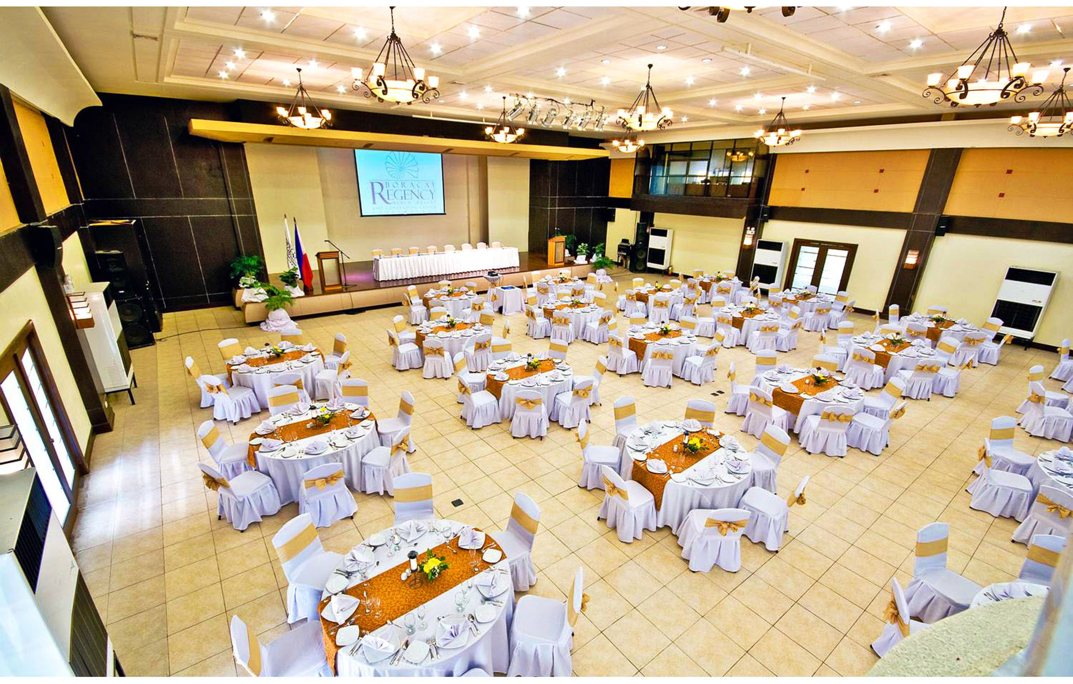 A large conference room with round tables and chairs, a podium, and a presentation screen.