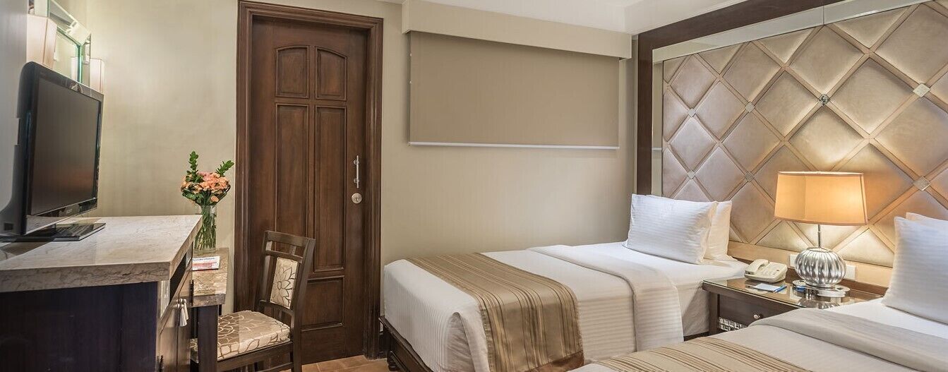 A hotel room with two beds, a desk with a computer, a chair, a TV, and a decorative vase.