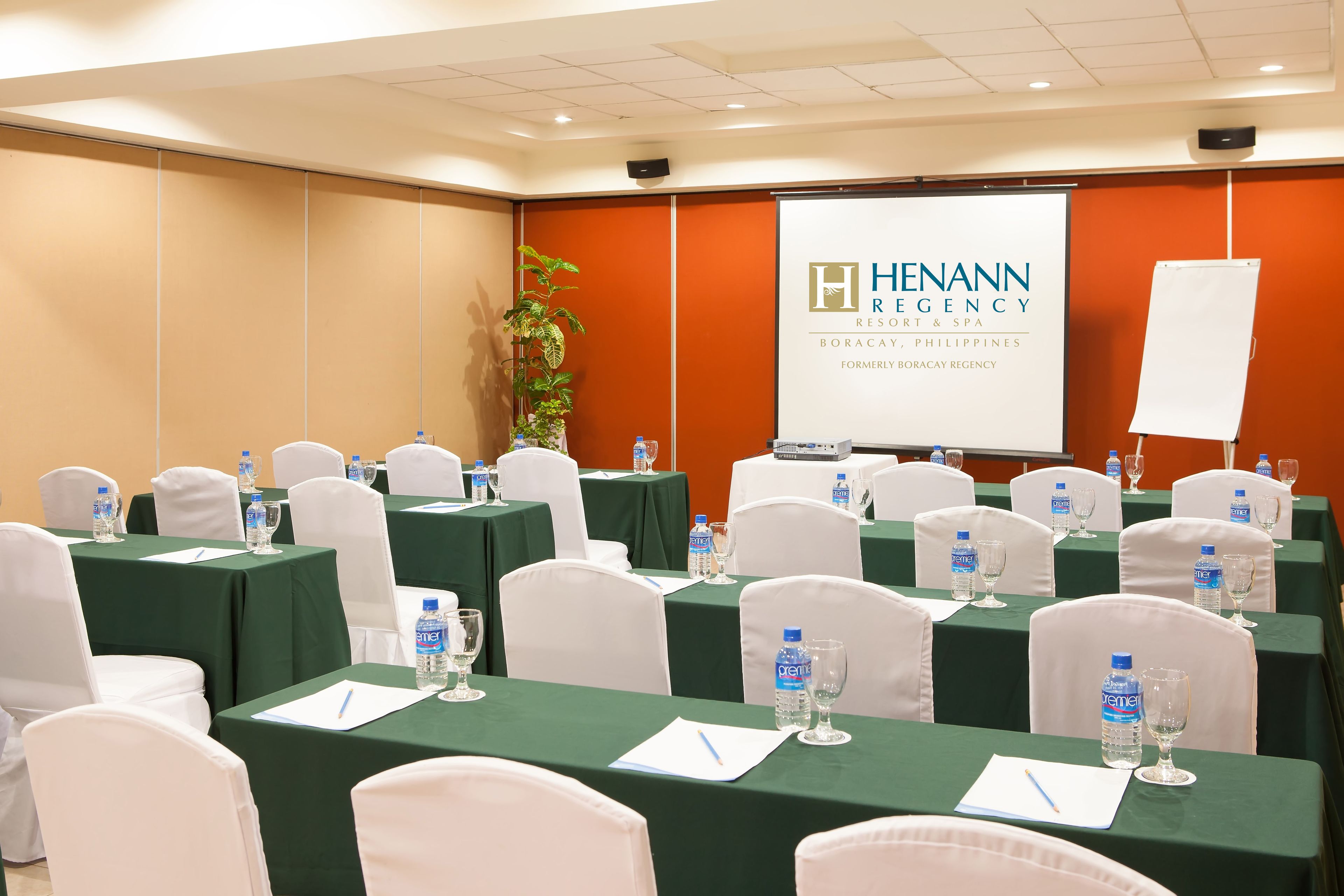A conference room with green tables, white chairs, water bottles, and a presentation screen displaying the logo of Henann Resort & Spa.