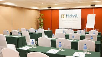 A conference room with green tables, white chairs, water bottles, and a presentation screen displaying the logo of Henann Resort & Spa.