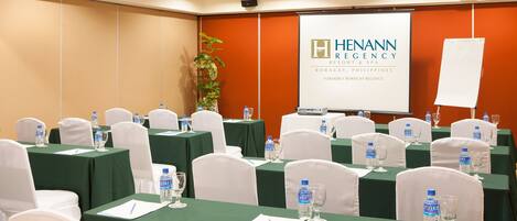 A conference room with green tables, white chairs, water bottles, and a presentation screen displaying the logo of Henann Resort & Spa.
