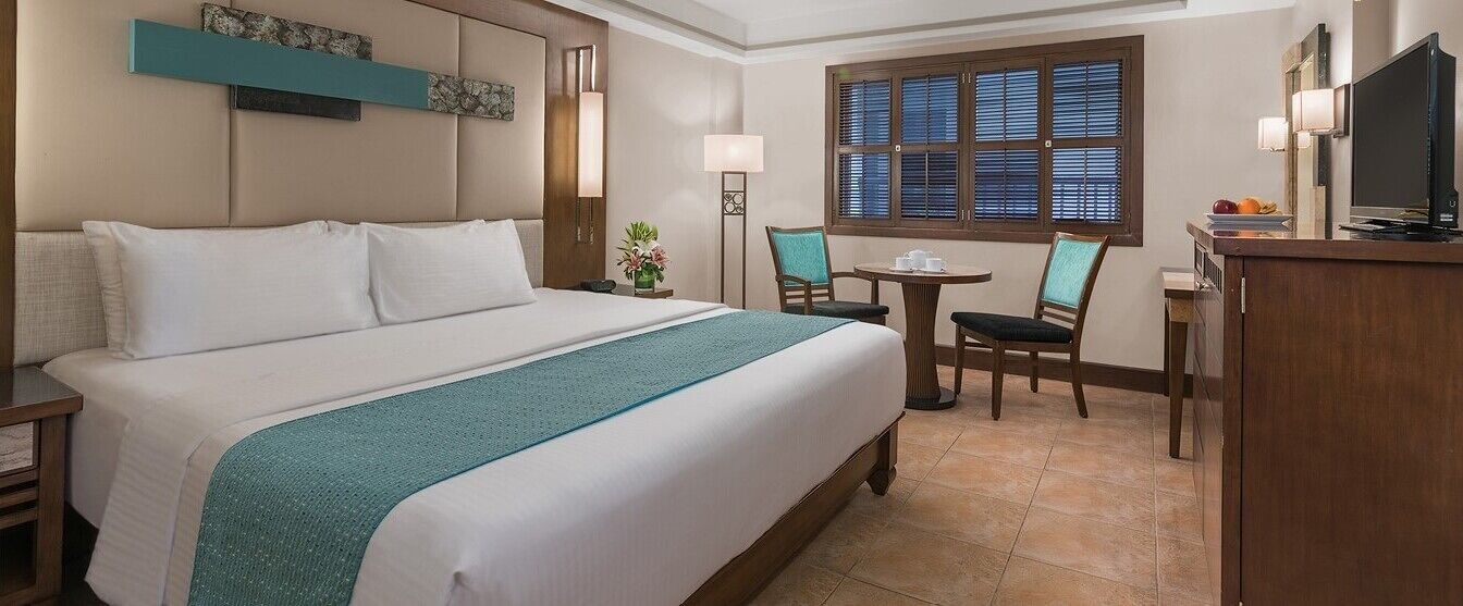 Una habitación de hotel con una cama grande, un escritorio con silla, televisión y ventana con persianas.