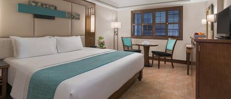 A hotel room with a large bed, a desk with a chair, a television, and a window with blinds.