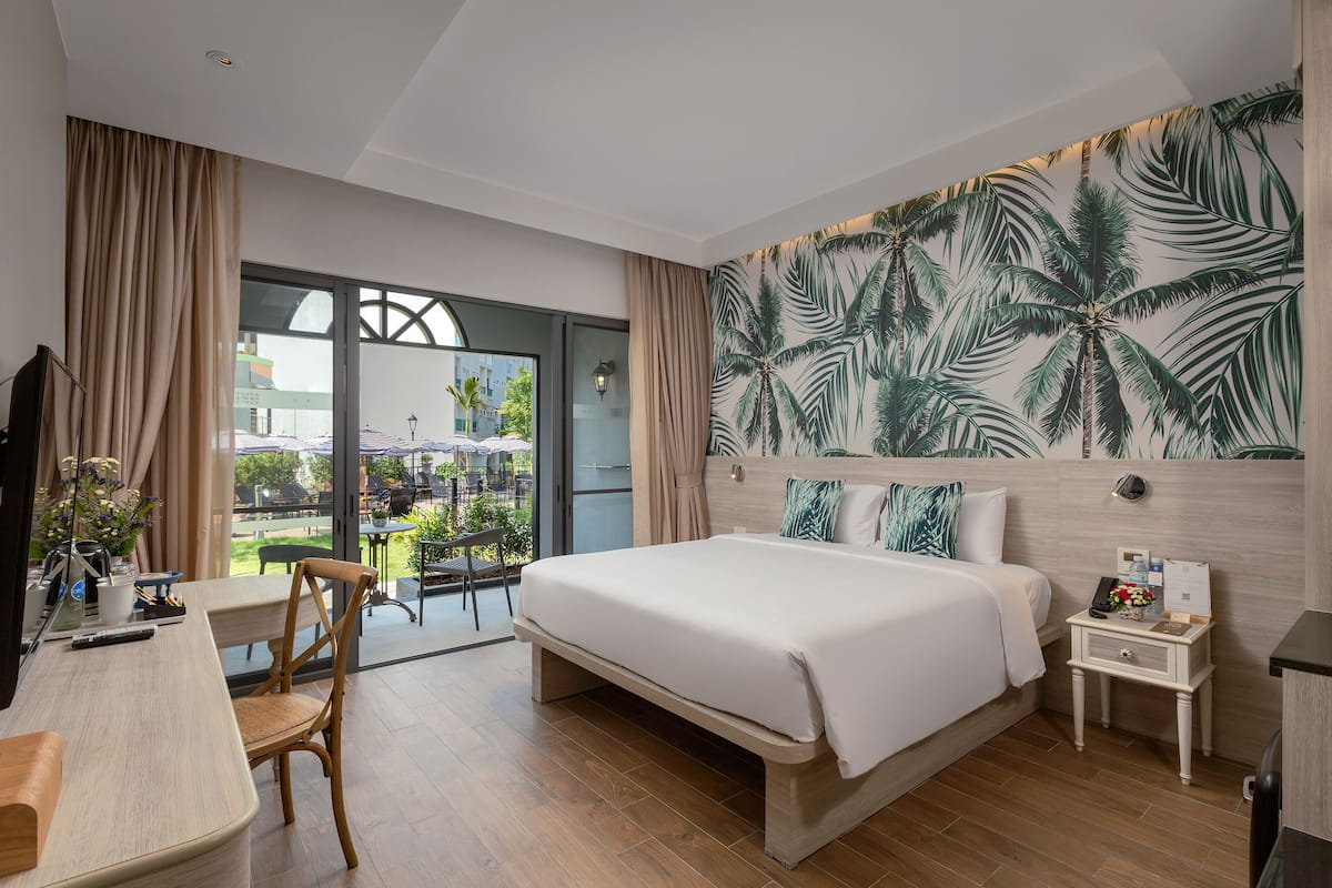 Una habitación de hotel moderna con una cama grande, un escritorio con silla, una mesita de noche pequeña y vistas al exterior.