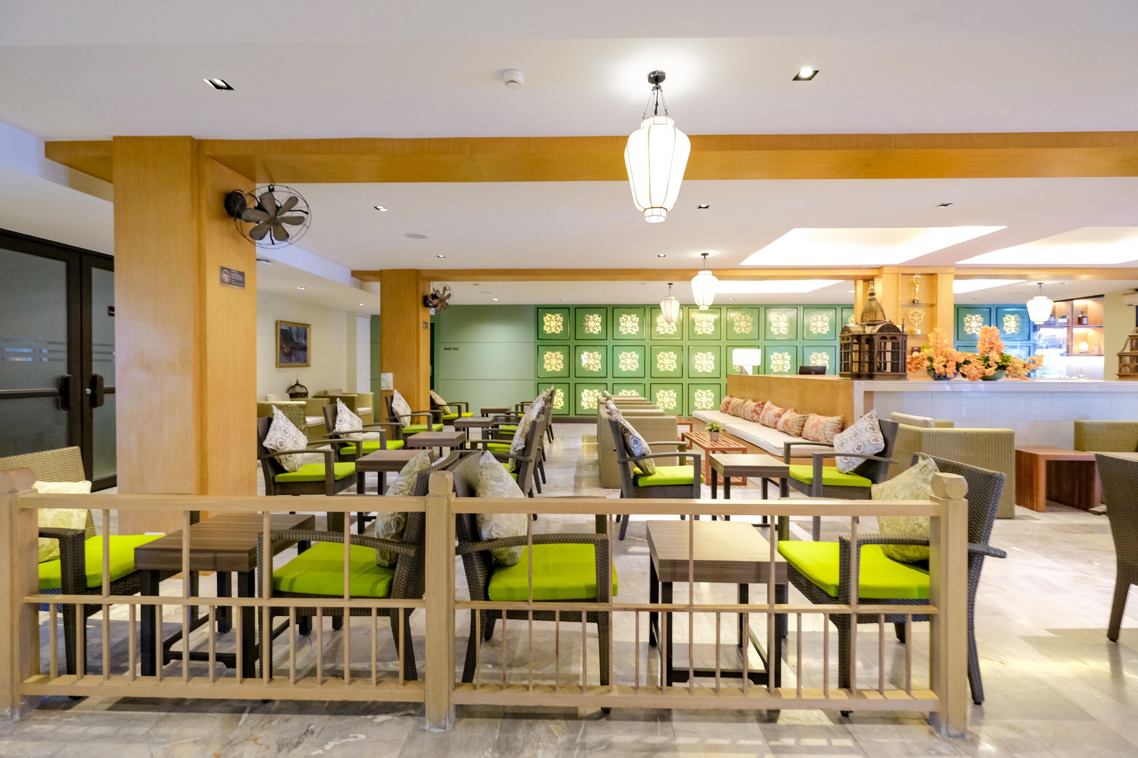 Een hotel lobby met meerdere zithoeken, inclusief banken en stoelen met groene kussens, een receptiebalie en een decoratieve wand met gepaneelde panelen.