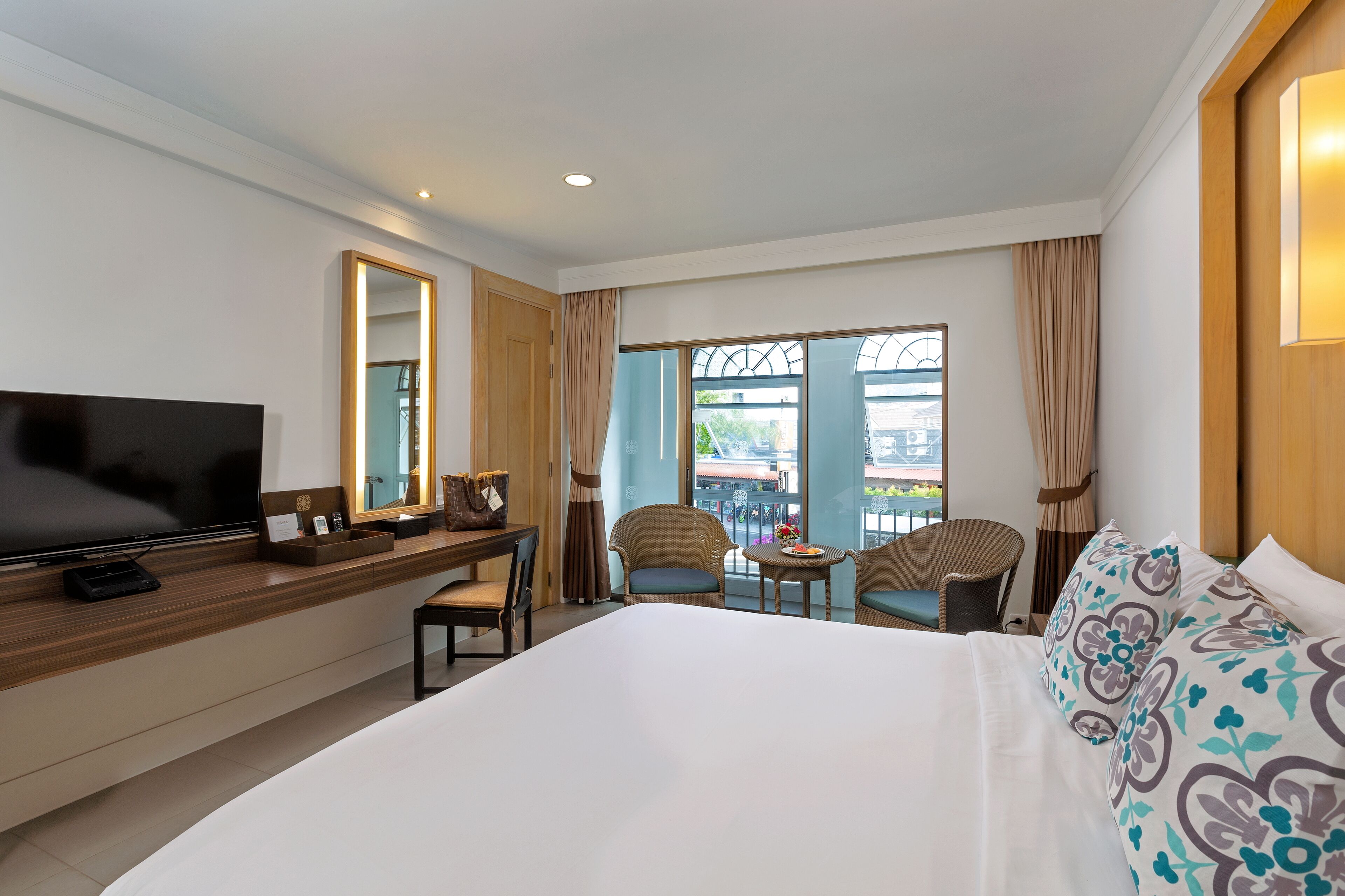 A hotel room with a large bed, a TV, a desk with a computer, a chair, and a small table.