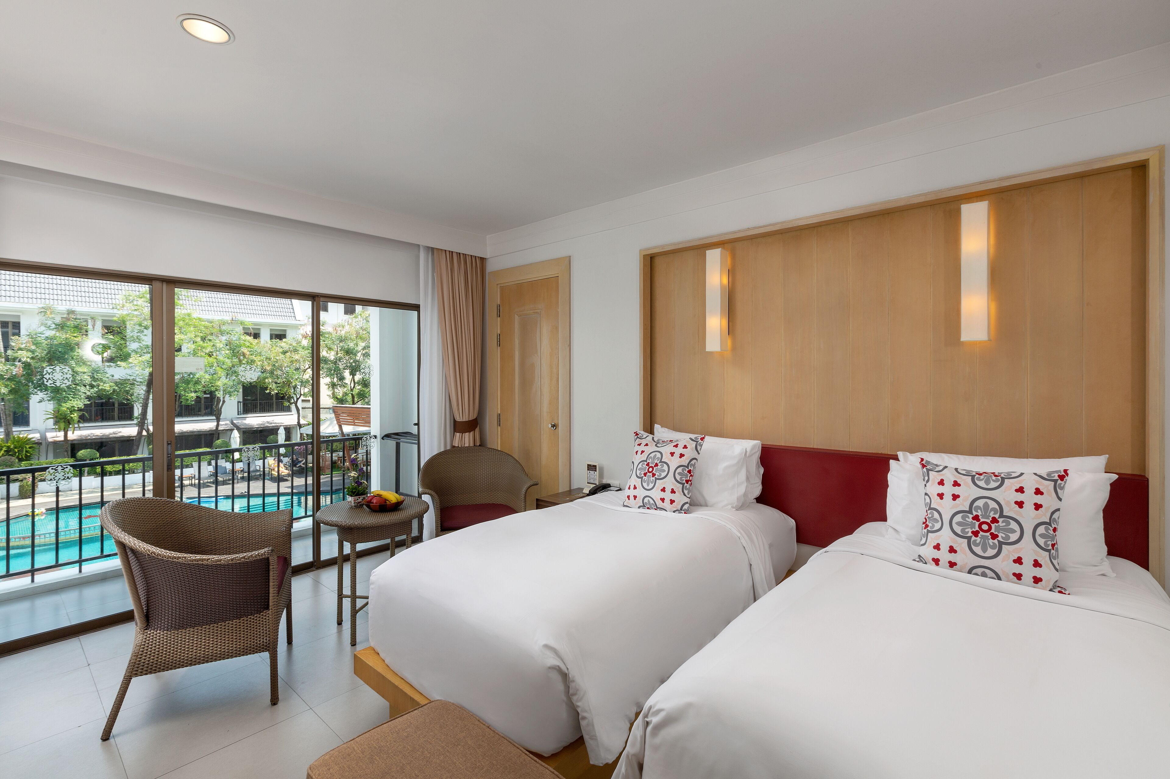 A hotel room with two beds, a balcony with a pool view, and a dining area with a chair and table.