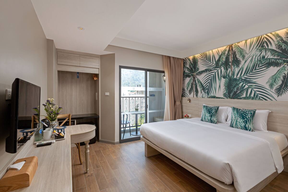 Habitación de hotel con cama, escritorio, televisor y balcón con vistas.
