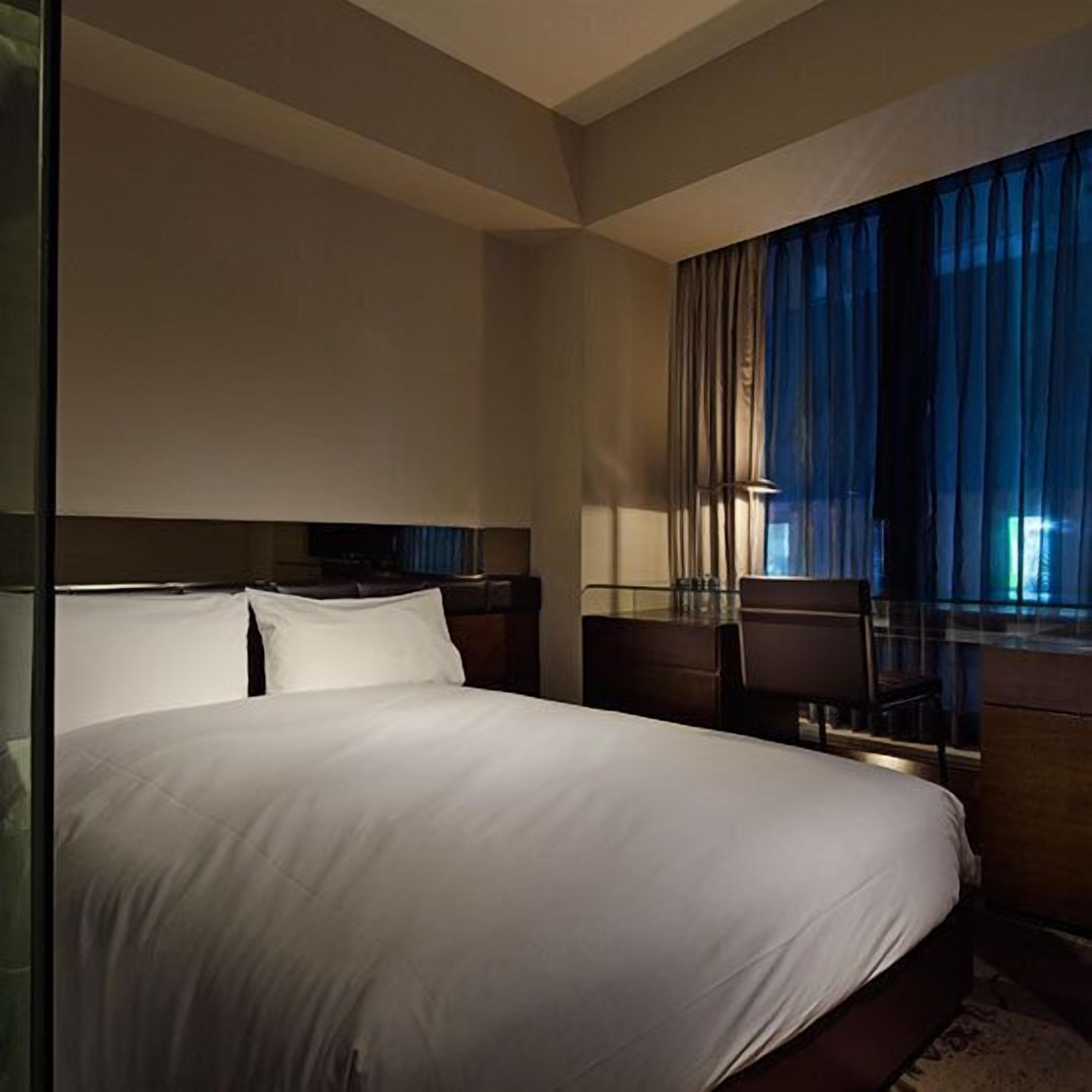A modern hotel room with a large bed, a desk, and a window with curtains.